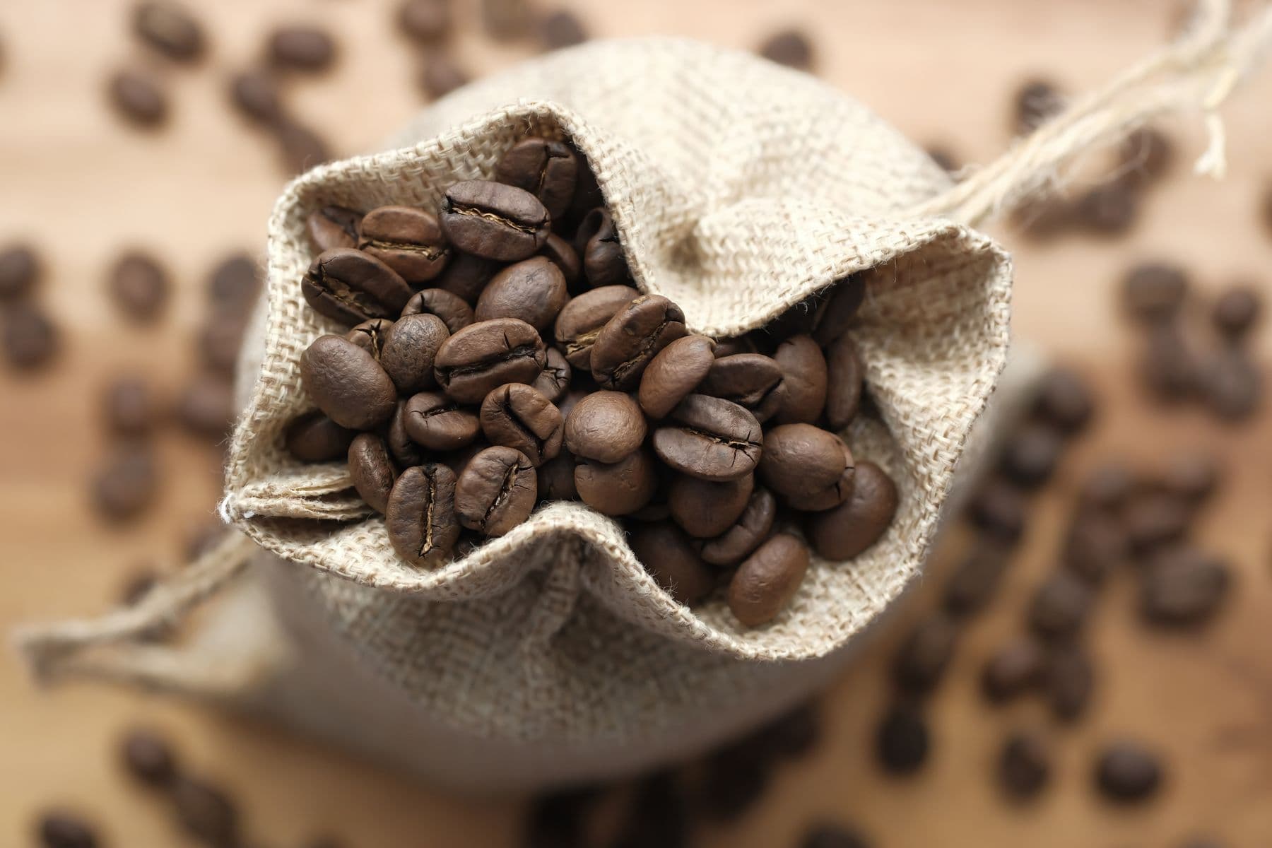 Fresh roasted coffee beans spilling from a natural linen bag